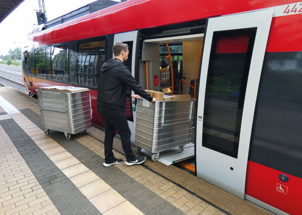 Ein Mann verlädt zwei Container mit Paketen über eine Rampe in einen Regionalzug